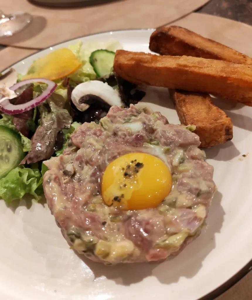 Tartare de bœuf traditionnel préparé au couteau avec son jaune d'œuf, accompagné de frites épaisses, spécialité du restaurant L'Atelier d'E&D.
